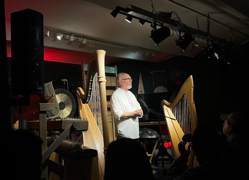 A performer on a stage standing between two harps