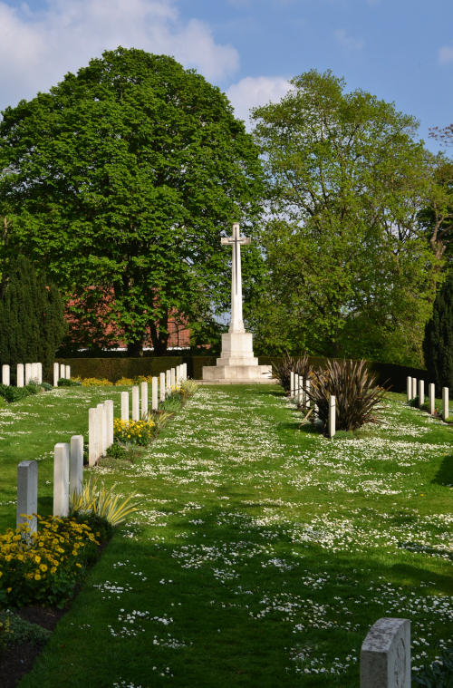 A military cemetery with graves set among grassland, and a stone cross at the far end