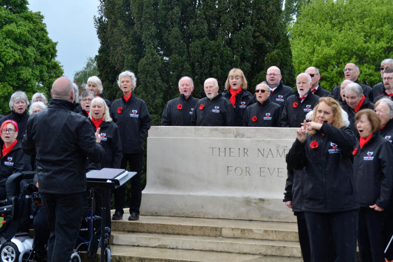 A group of singers gathered around the large memorial stone at Tyne Cot Cemetery