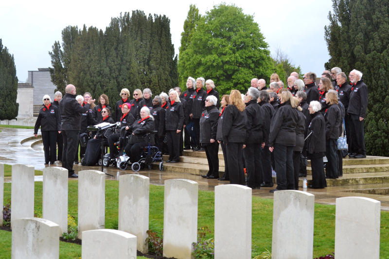 A group of singers singing outdoors, with a row of grave headstones in the foreground