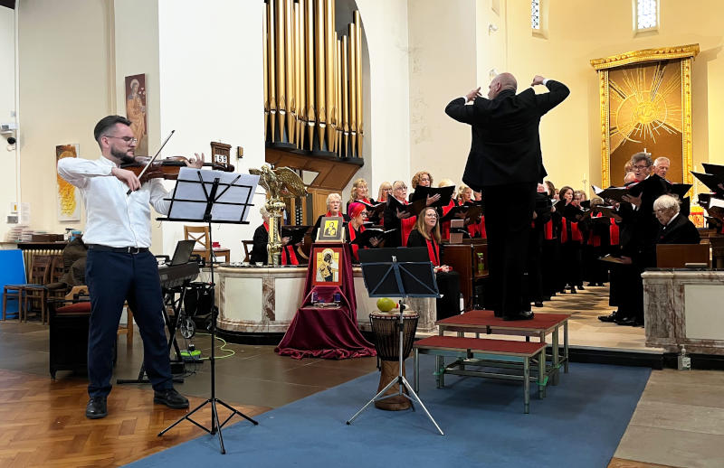 A solo viola player performs at the front of a church, while conductor James Llewellyn Jones leads a choir