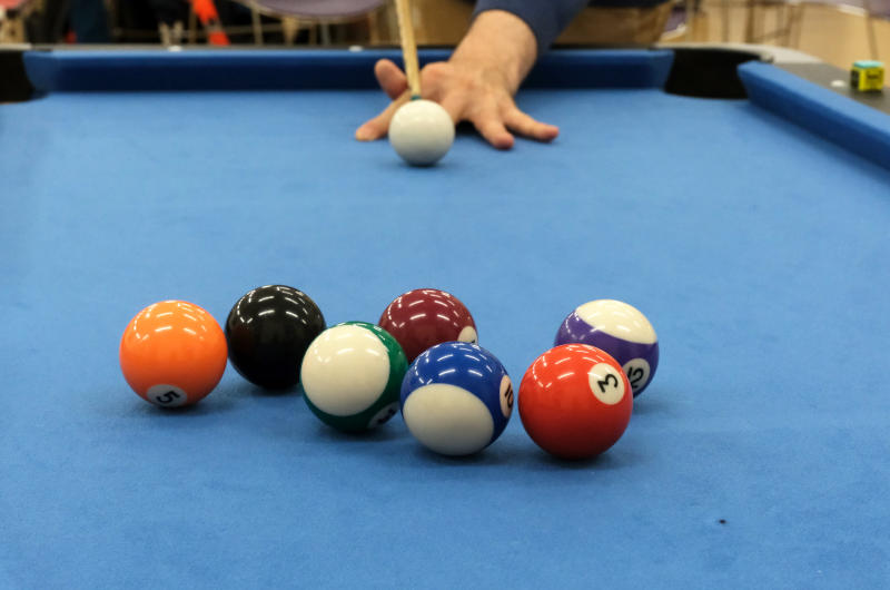 A pool table, with a cue at the far end about to send the cue ball towards a group of balls at the near end