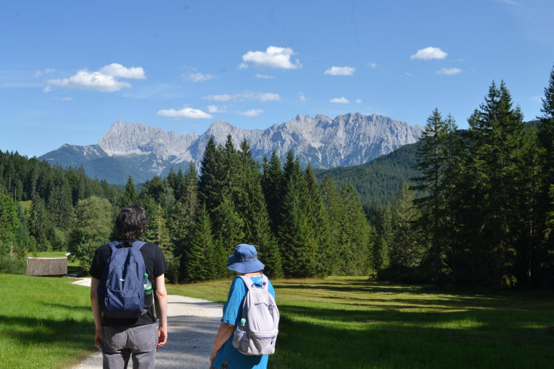 Martin and Miriam walking along a path in sunshine, with trees and mountains in the background