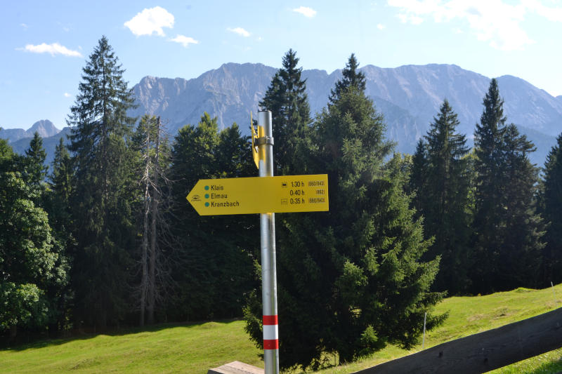 Yellow signpost, with trees and mountains in the background, pointing the way to Elmau and Kranzbach