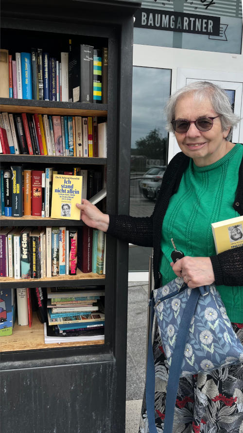 Miriam holding Else's book "Ich stand nicht allein" in front of a bookcase