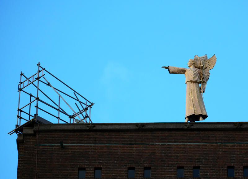 Statue of an angel with sky in the background, pointing at a section of scaffolding