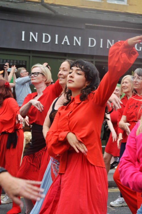 People wearing red dresses performing dance maneouvres in a street
