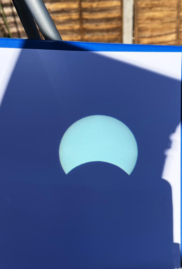 Image of the Sun projected on to a piece of white paper, with the shadow of the Moon eating into one side of the Sun's disk